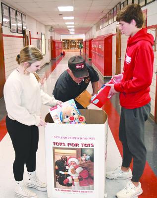 Albany High School students Maddie Stapp (l) and Cade Fairchild (r) help Marine SSgt. Doug Beaty (c), who picked up toys and about $600 here last week for the Toys for Tots program. Pickup is set for Dec. 17-18 at the Youth Center. DONNIE LUCAS / ALBANY NEWS